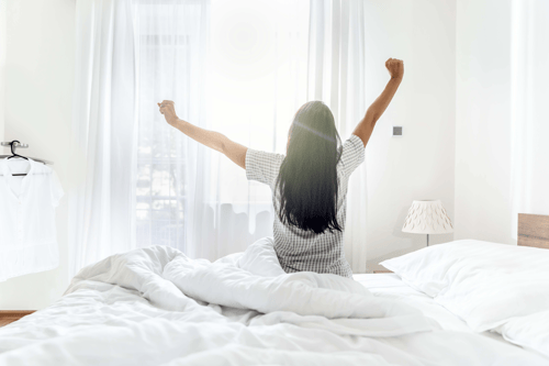 Eine Frau streckt sich im Bett am Morgen.